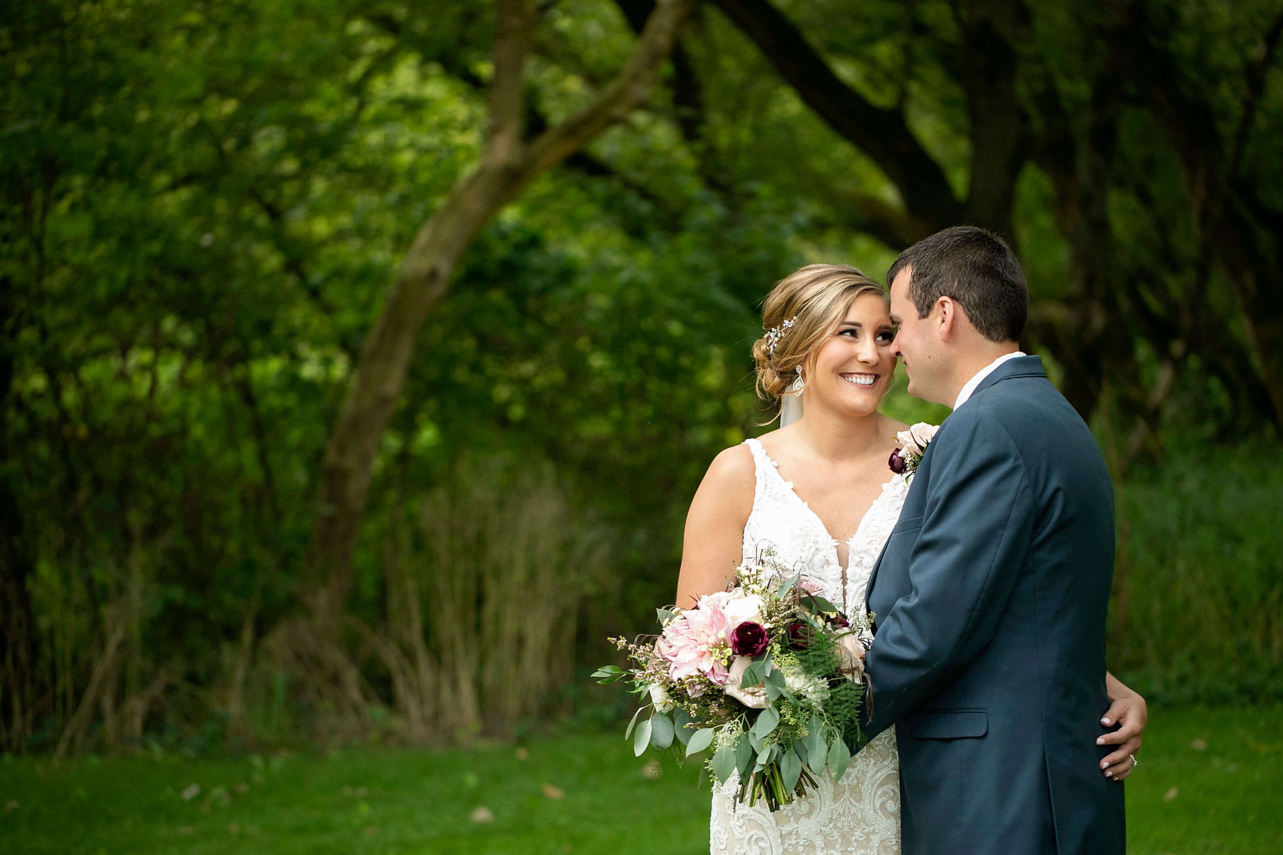 Newlyweds share tender moment surrounded by green foliage in garden setting.