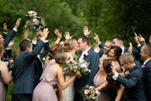 Wedding party celebrates with raised hands during outdoor group photo.