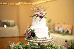 Elegant white tiered wedding cake decorated with pink roses and greenery on silver stand.
