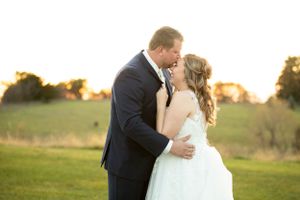 Newlyweds embrace in golden sunset light on grassy field during romantic moment.