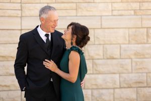 A couple sharing an intimate moment while dressed in formal attire against a stone wall.