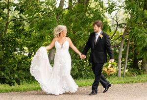 A couple walks hand in hand on a path surrounded by lush green trees and nature.