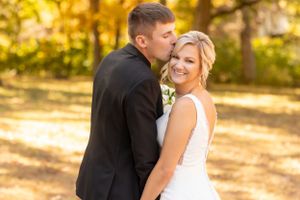 Romantic autumn wedding portrait captured in golden sunlight among fall foliage.
