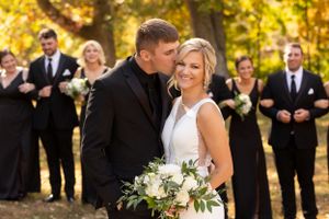 Wedding party in black and white attire poses outdoors during fall season.