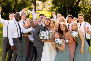 Large wedding party celebrates with joyful expressions in sun-drenched outdoor setting.