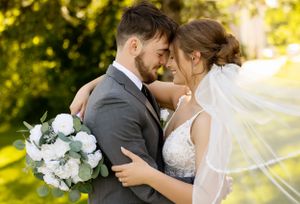 An intimate moment between newlyweds with flowing veil and white bouquet in golden outdoor lighting.