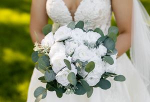 An elegant white and eucalyptus wedding bouquet with lace dress detail.