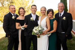 Wedding party in formal attire poses together outdoors holding white floral bouquets.