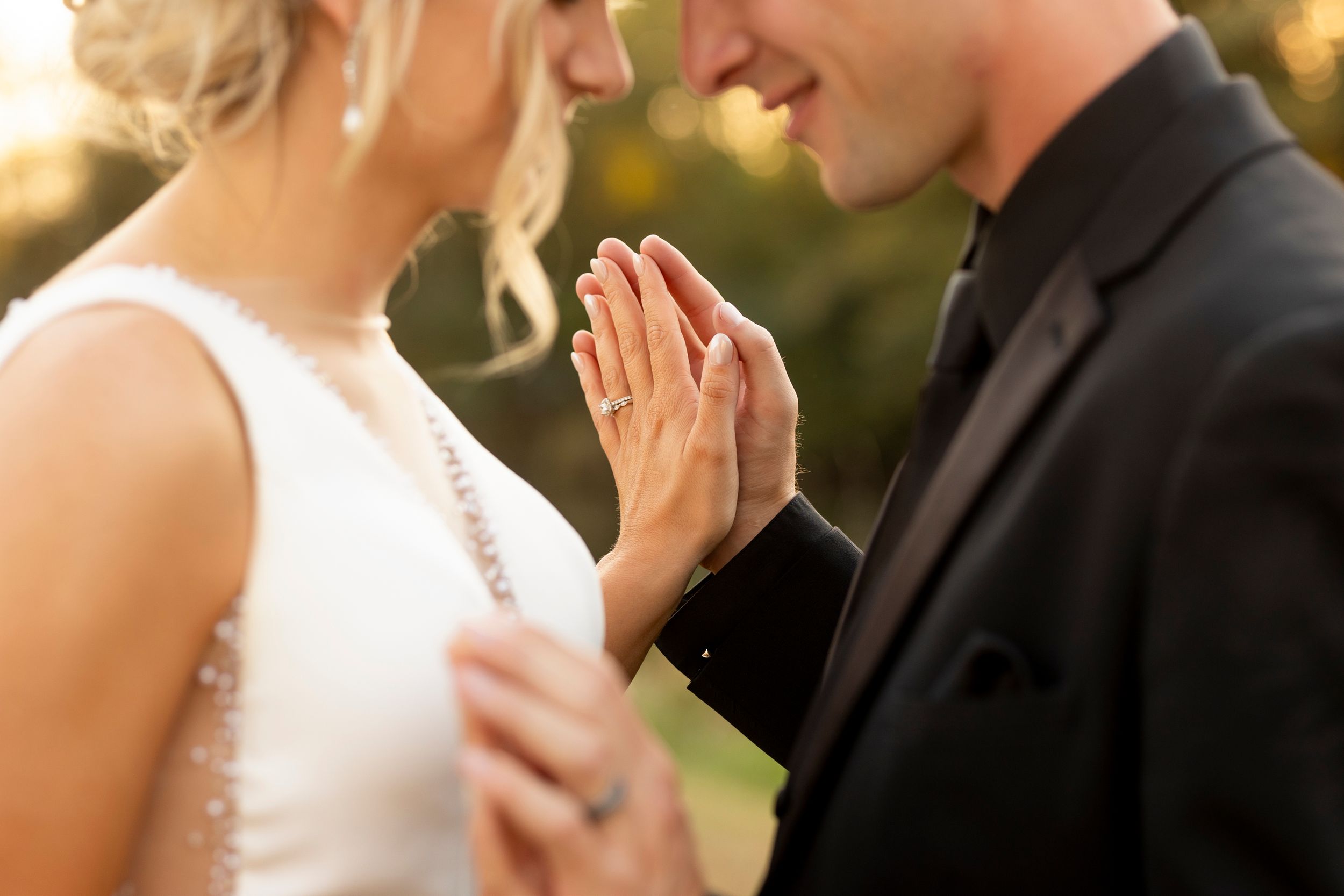 Intimate moment between couple showing wedding rings and formal attire during sunset.