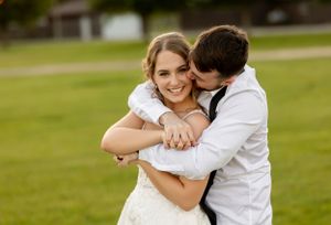 A playful embrace between newlyweds on their wedding day in a grassy field.
