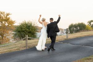 Newlyweds celebrate with raised arms while walking down a path together.