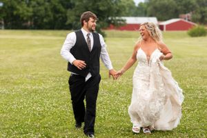 A joyful couple runs together across a grassy field with a red barn in the background.