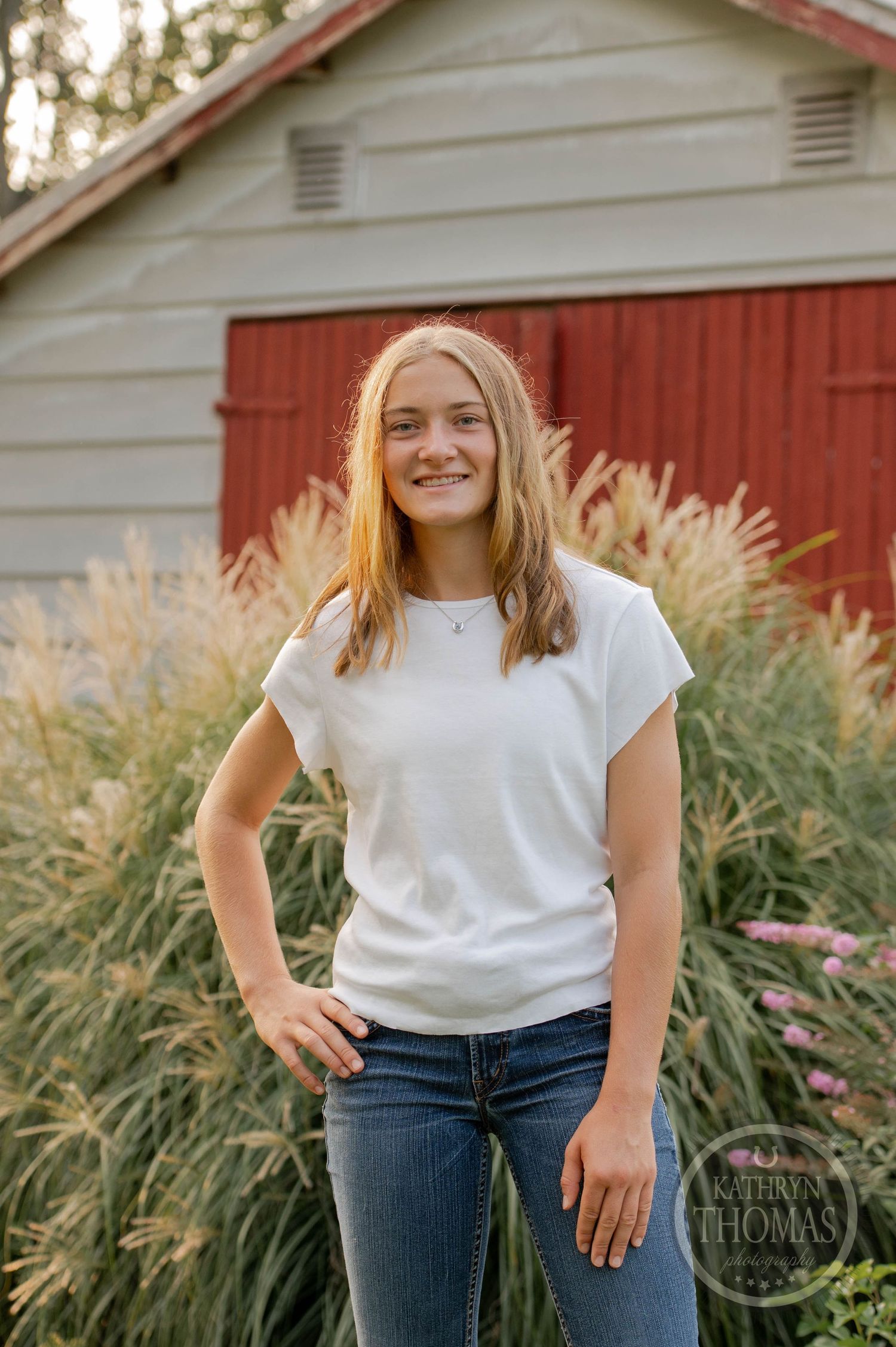Portrait against a red barn with ornamental grasses in warm evening light.