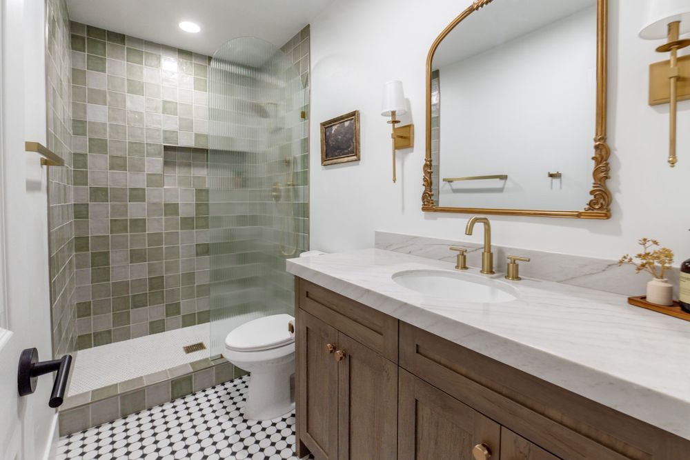 Contemporary bathroom featuring green tile shower, patterned floor, and wooden vanity with gold fixtures. MLS Photographer, Phoenix Arizona
