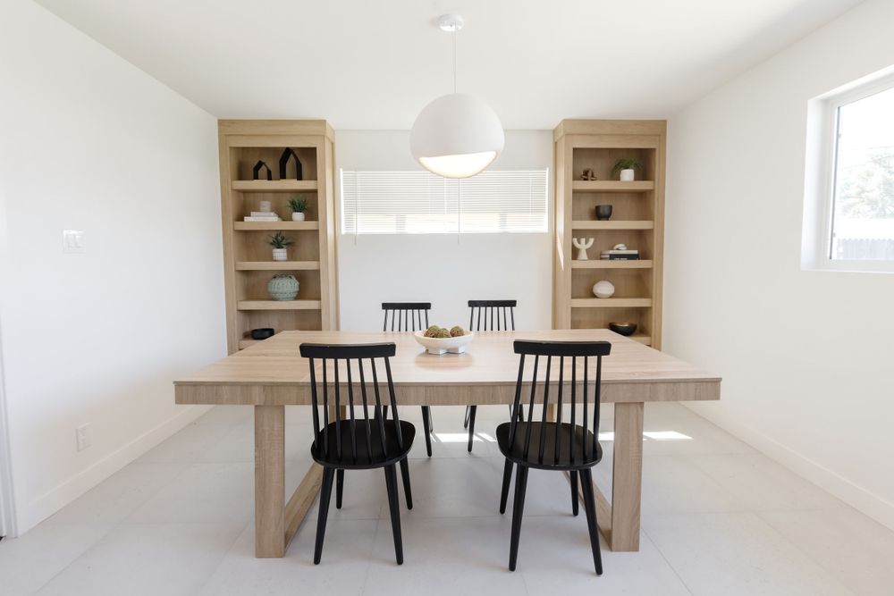 Minimalist dining area with wooden table, black chairs, and built-in shelving displaying ceramic dishes. MLS Photographer, Phoenix Arizona