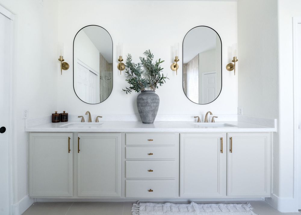 Elegant double vanity bathroom with oval mirrors, brass sconces, and white cabinetry. MLS Photographer, Phoenix Arizona
