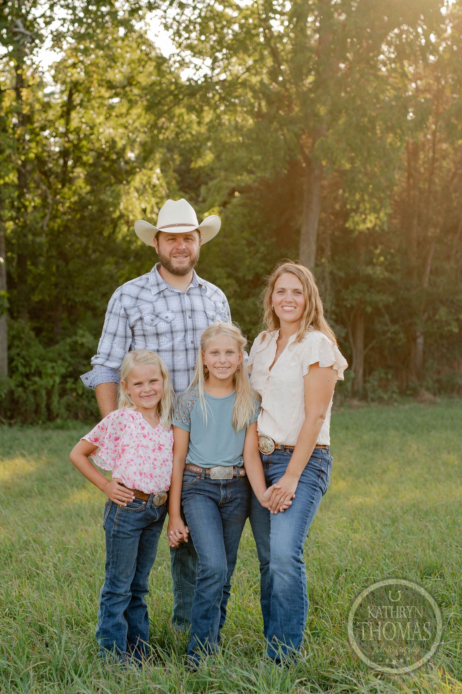 Western-styled family portrait in a grassy field during golden hour.