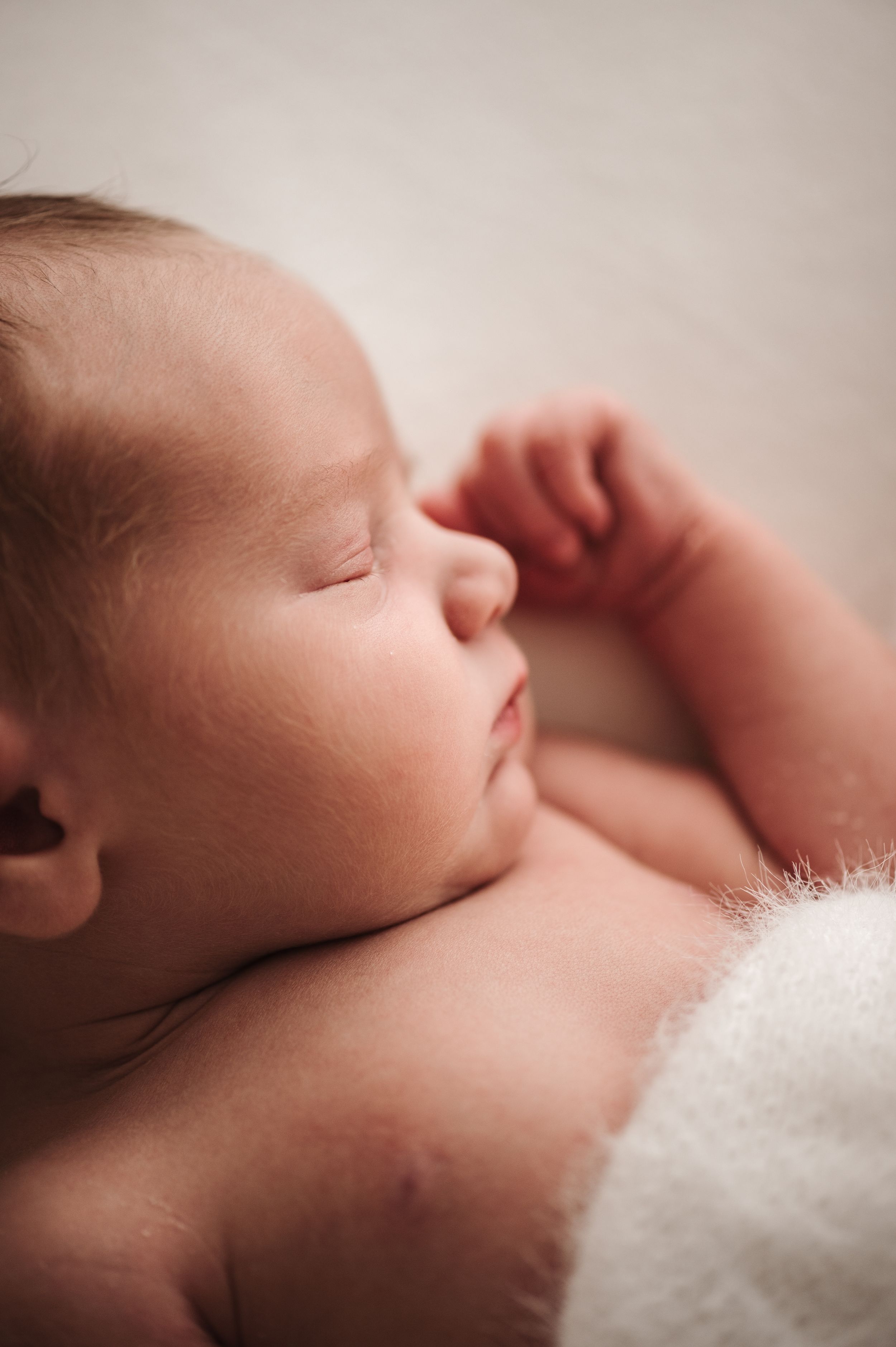 Peaceful sleeping newborn close-up with soft white blanket.