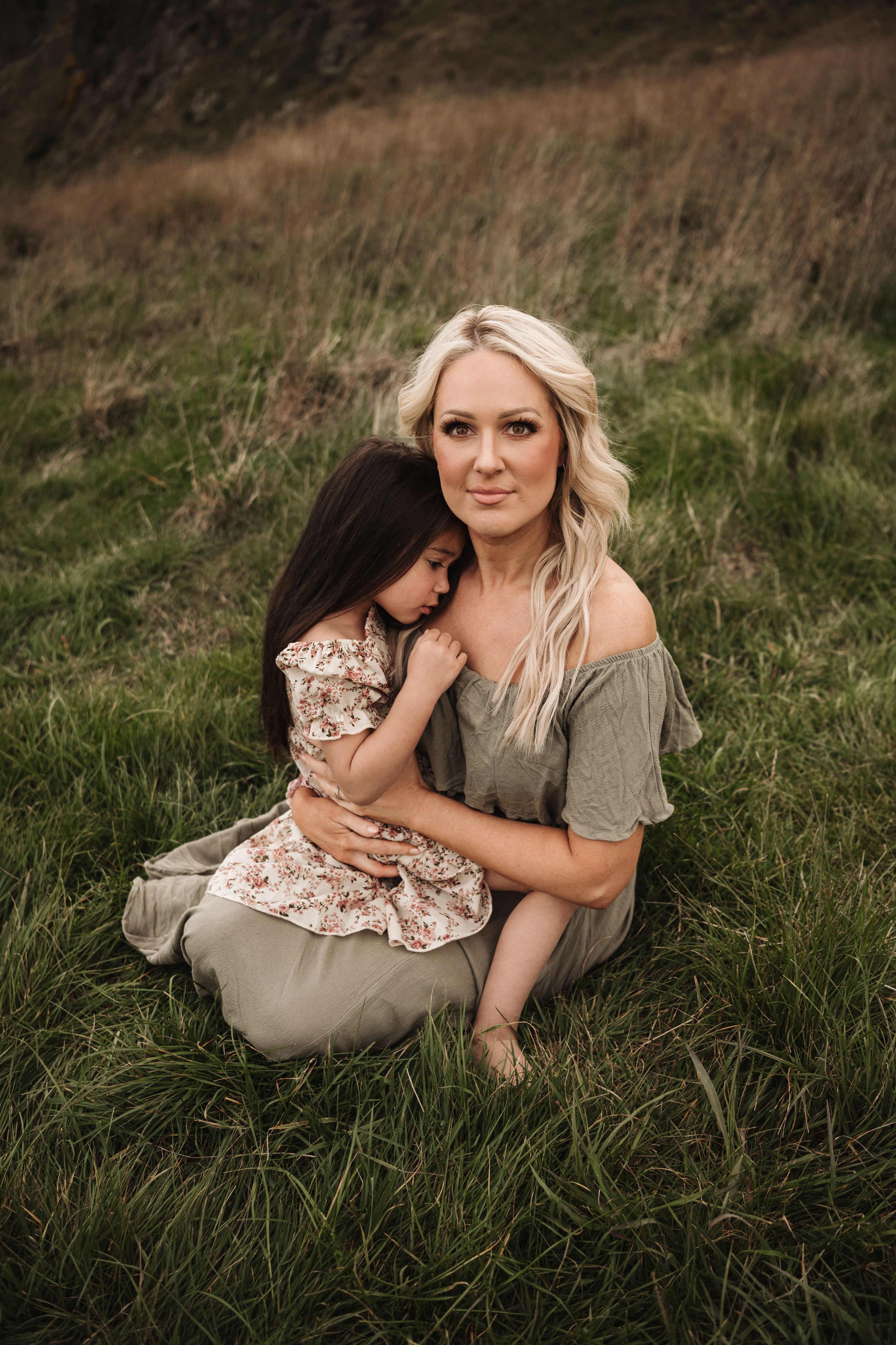 Heartfelt outdoor portrait of mother and child embracing in tall grass at sunset.
