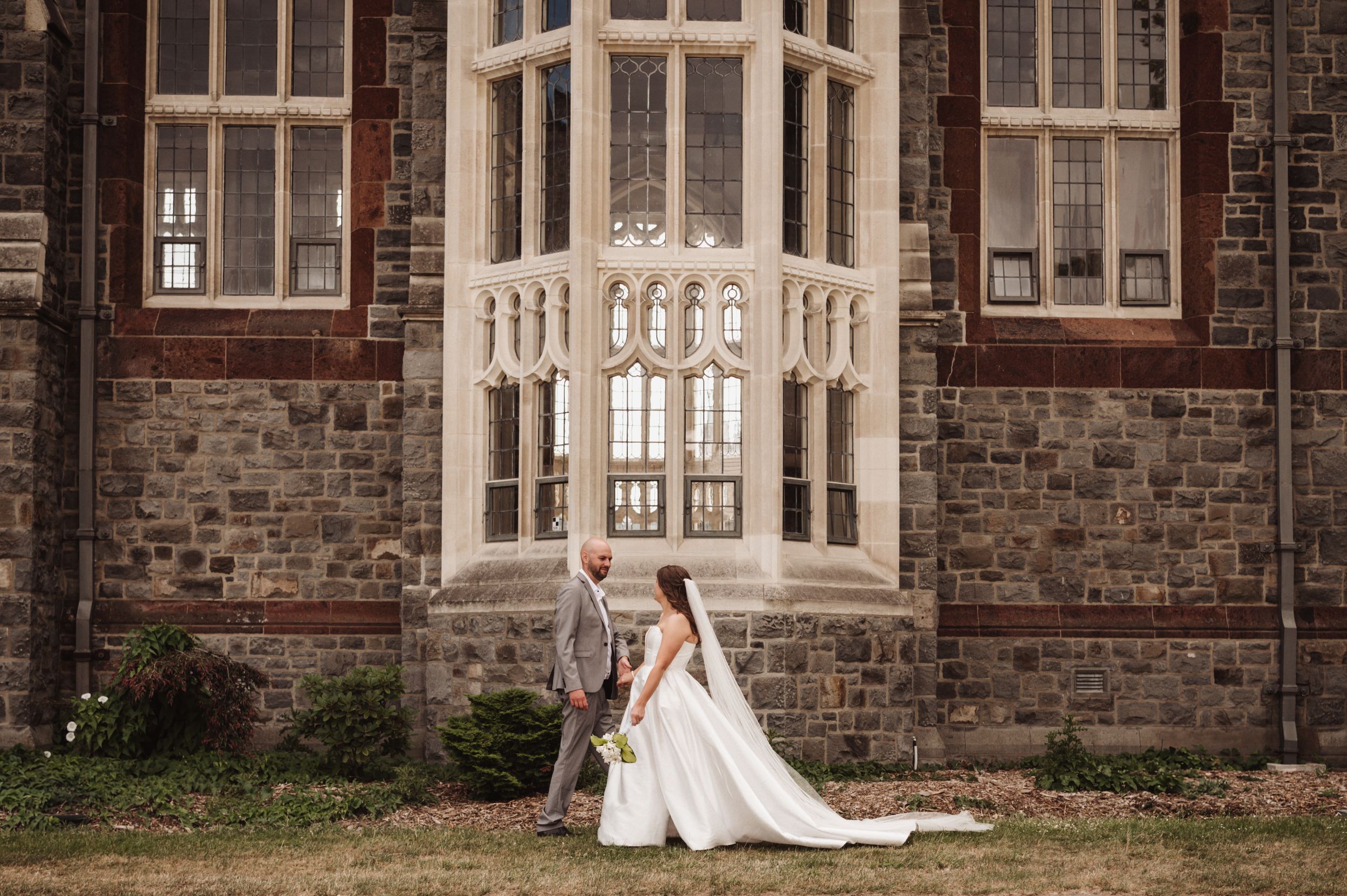 Wedding portrait in front of ornate stone building with Gothic architecture.