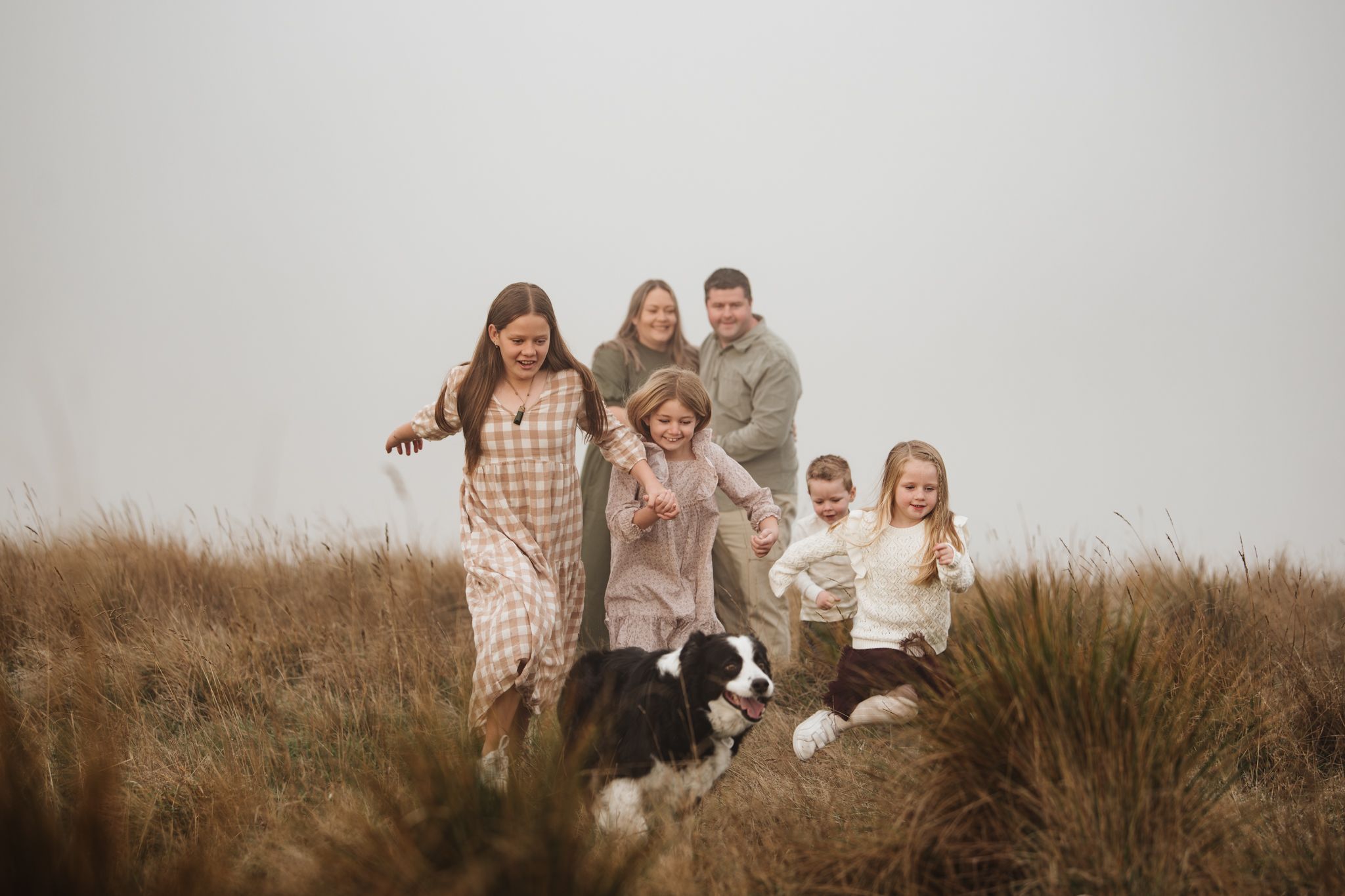 Family with dog posing together on misty hilltop among tall grass.