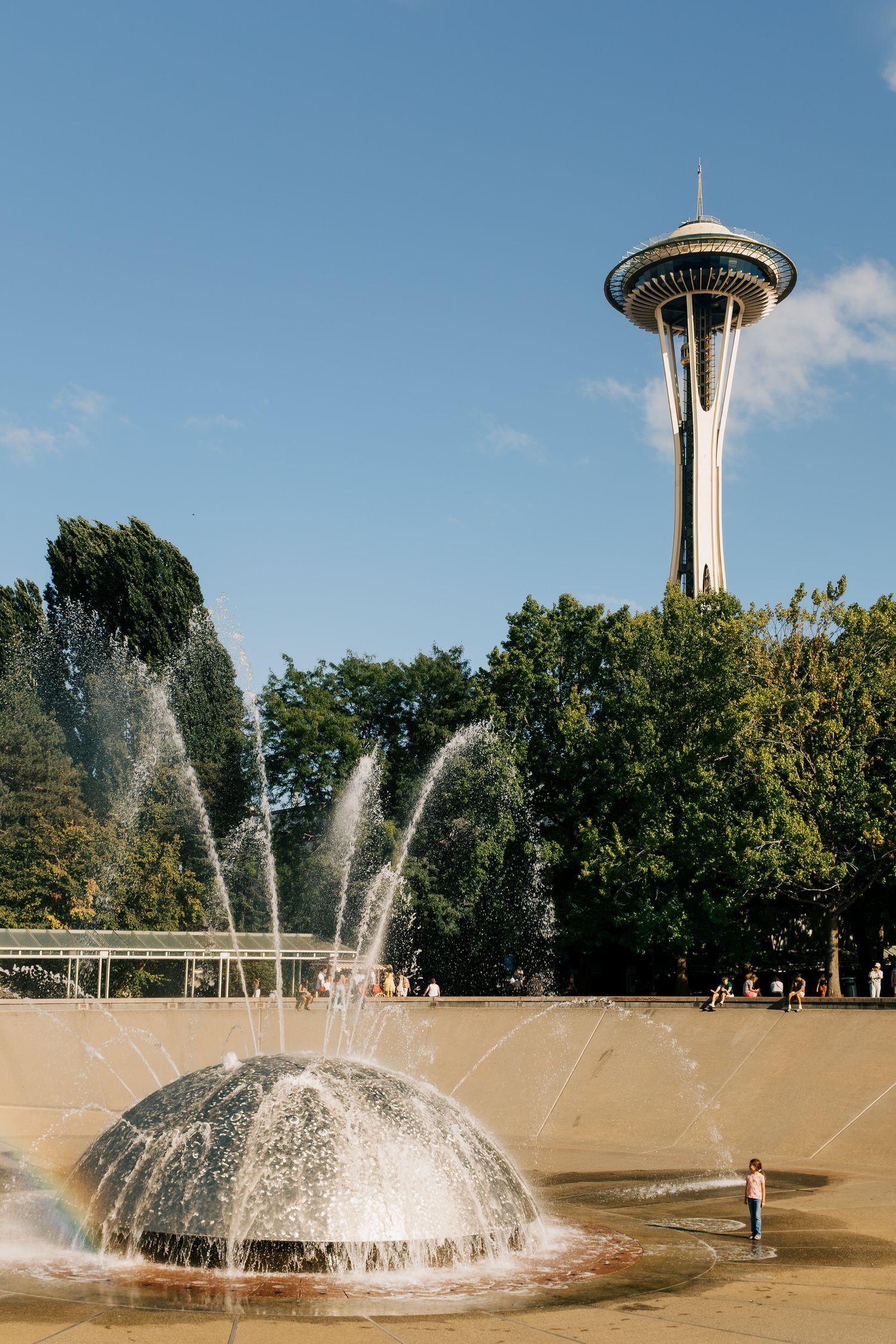 Seattle's Space Needle towers over a fountain display in a sunny urban park.
