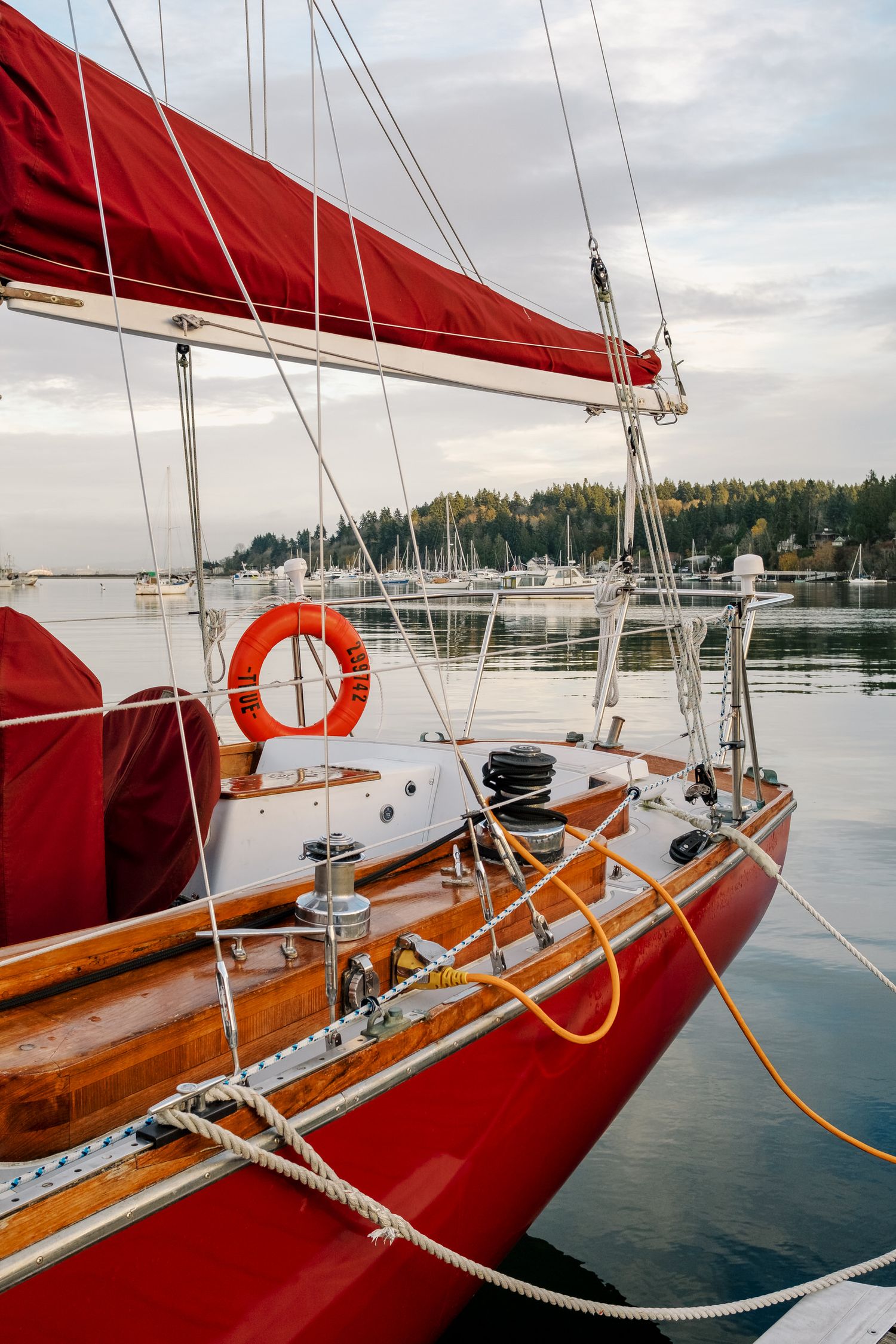 Red-sailed vintage sailboat moored at a peaceful marina with life preserver and wooden details visible.