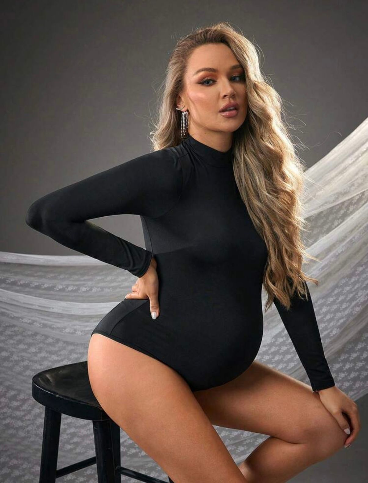 Studio maternity photoshoot featuring a black bodysuit against a dark background.
