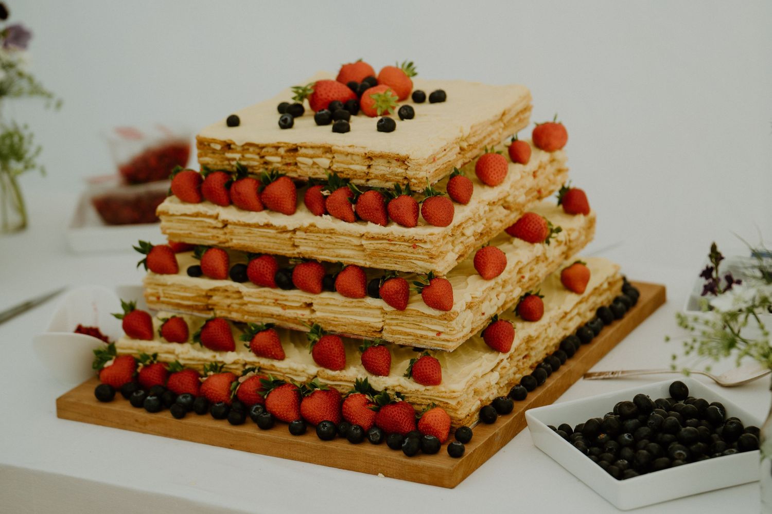 A tiered rectangular wedding cake decorated with fresh raspberries and blueberries on a wooden base.