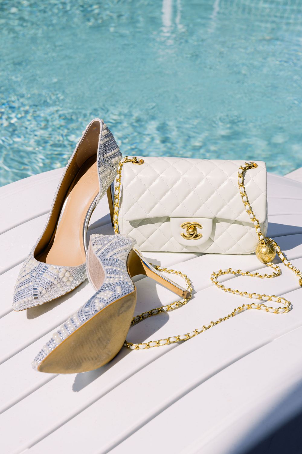 Sparkly silver wedding shoes and white quilted designer purse displayed by pool.