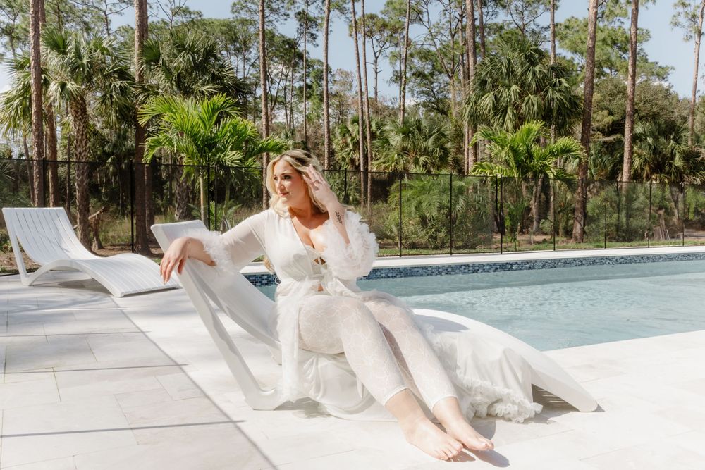 White-robed figure relaxing on lounge chair by modern pool surrounded by palm trees.