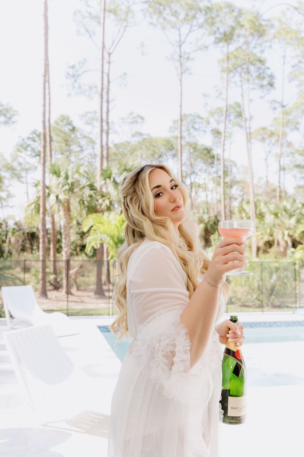 Poolside celebration with champagne and cocktail against tropical forest backdrop.