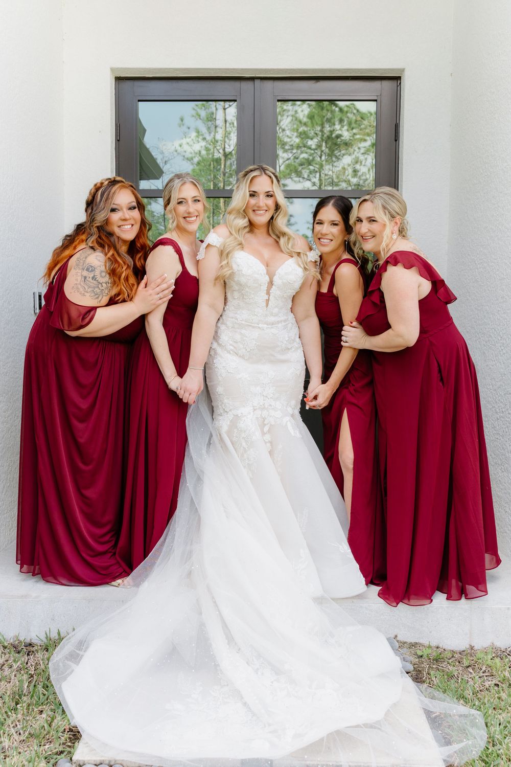 Bridal party gathers for formal photo with bridesmaids in deep red dresses.