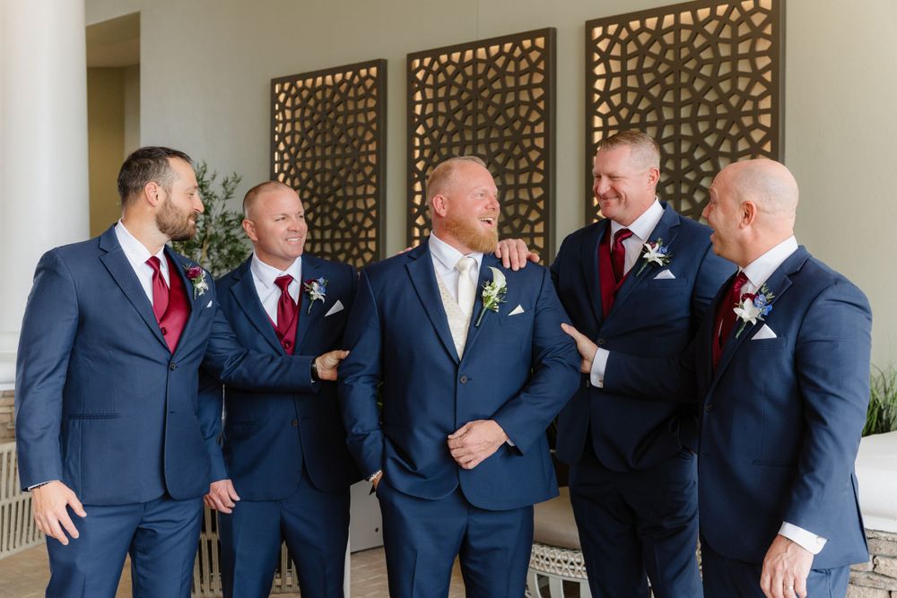 Groomsmen in navy suits share a laugh against decorative wall backdrop.