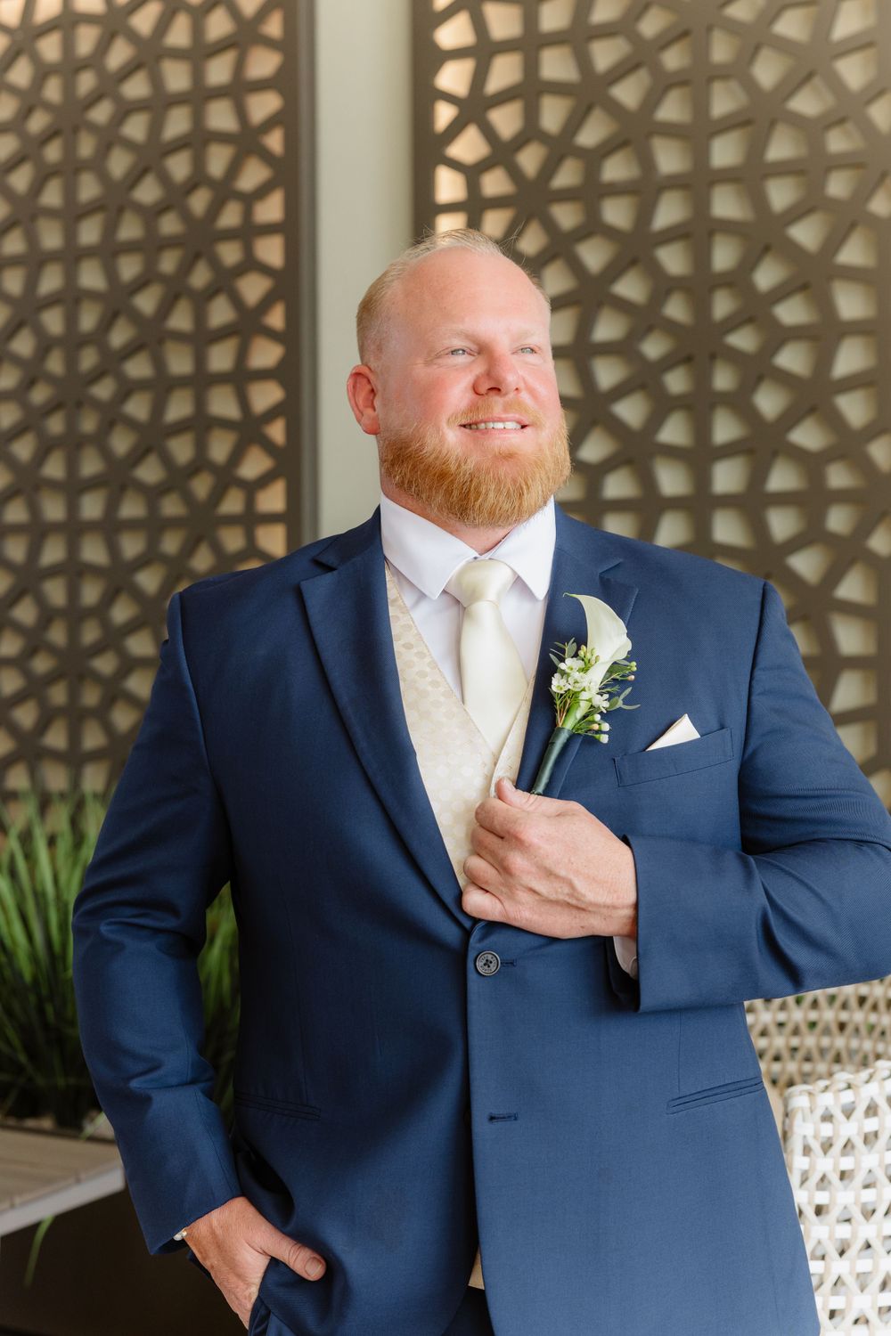 Groom in navy suit with boutonniere poses against geometric patterned wall.