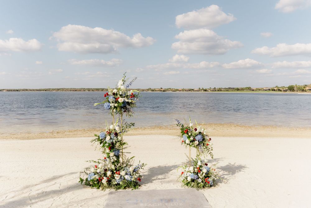 Two floral arch arrangements on a sandy beach overlooking a serene waterfront.