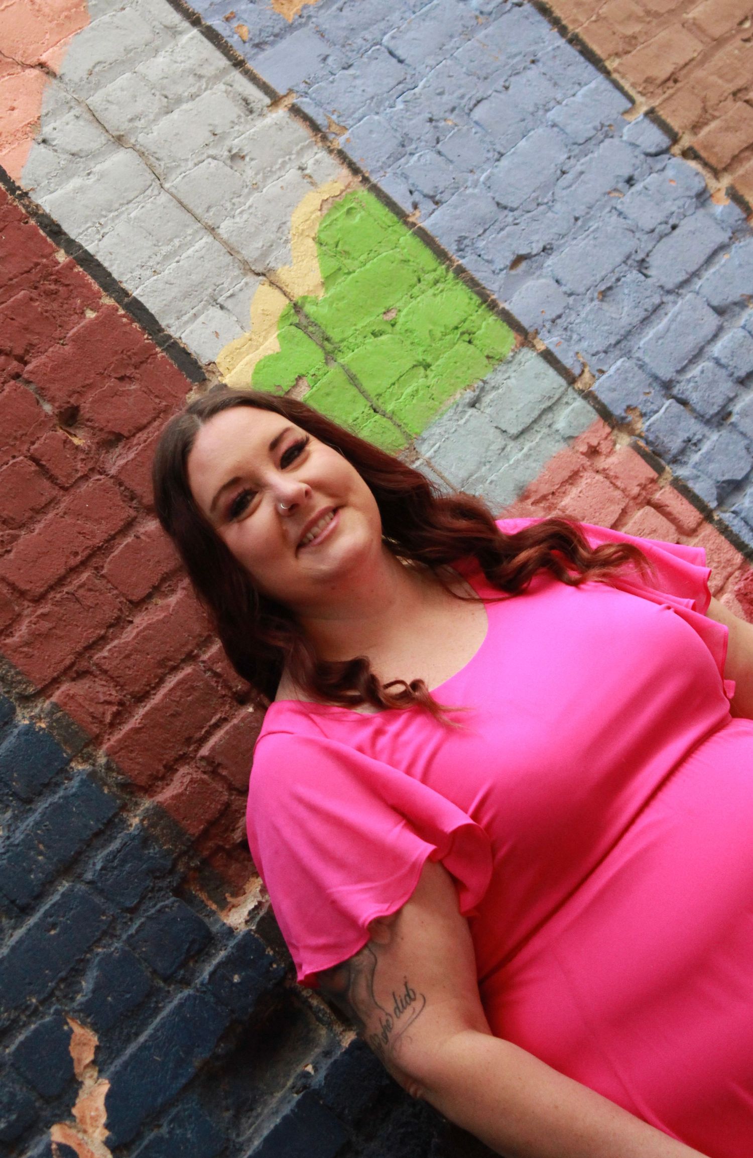A person in a bright pink top poses against a multicolored brick wall background.