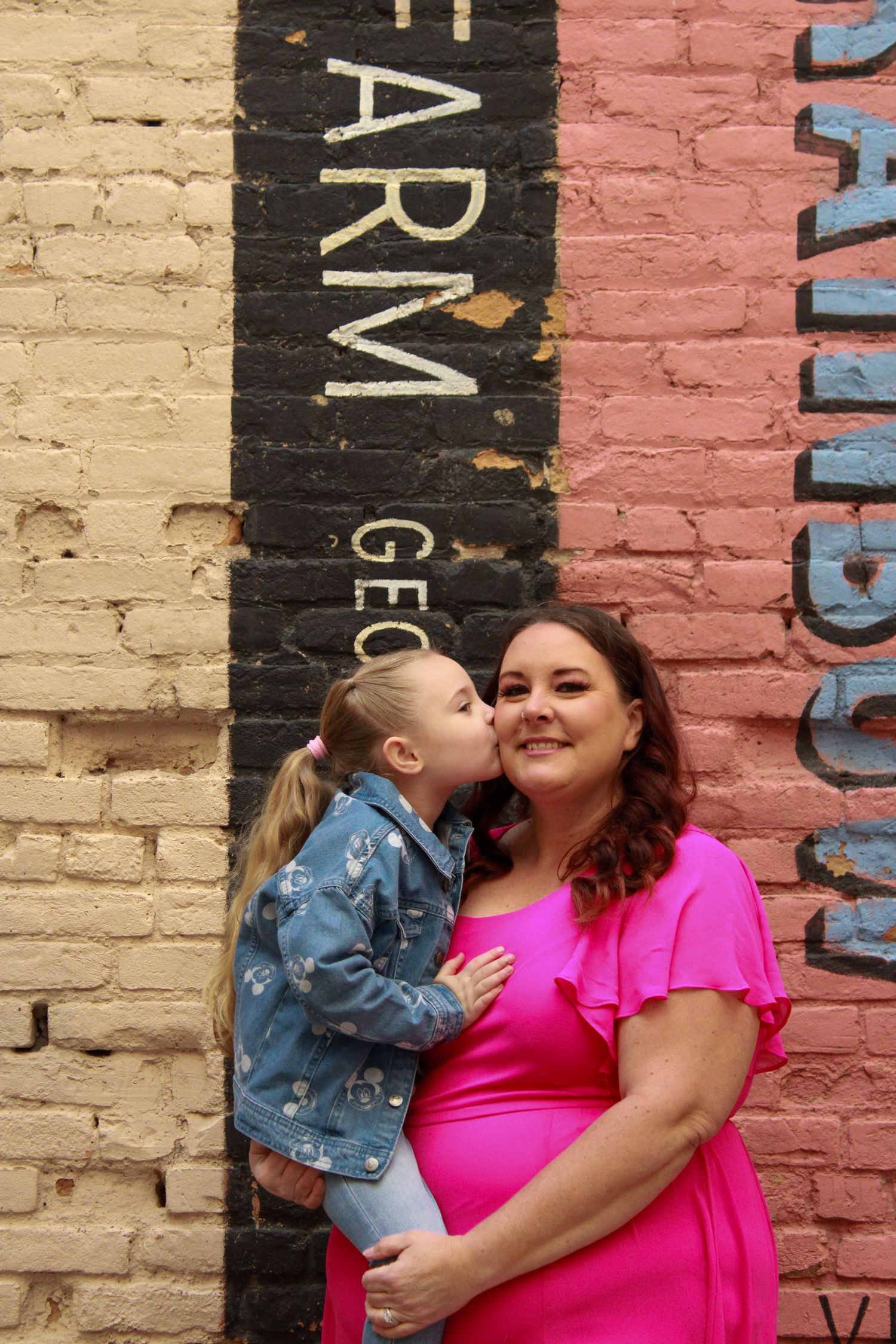 A sweet moment captured against painted brick wall with black text reading FARM.