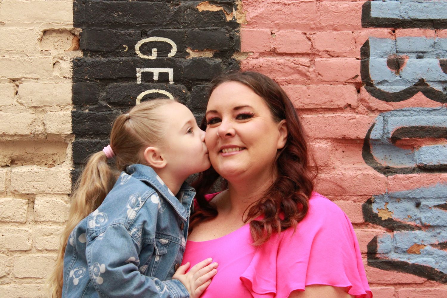 A tender moment shared between two people against colorful painted brick wall background.