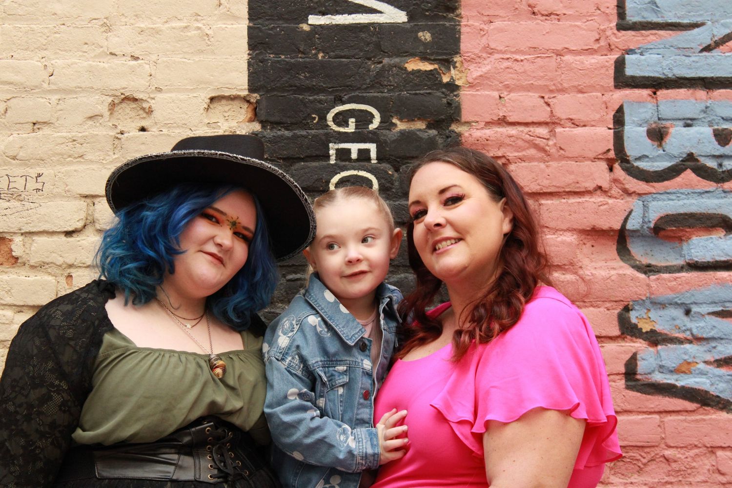 Three figures pose together against a painted brick wall with vintage text elements.