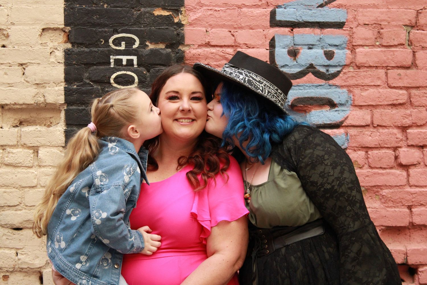 A family poses together against a colorful brick wall background with painted lettering.