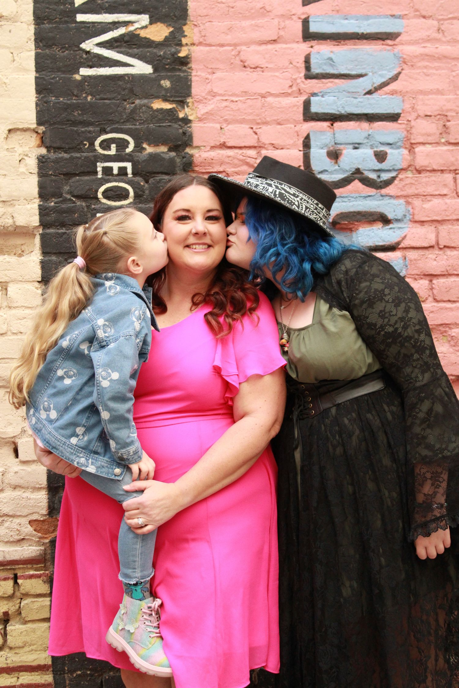 A group photo against colorful brick wall featuring casual outfits and warm embraces.