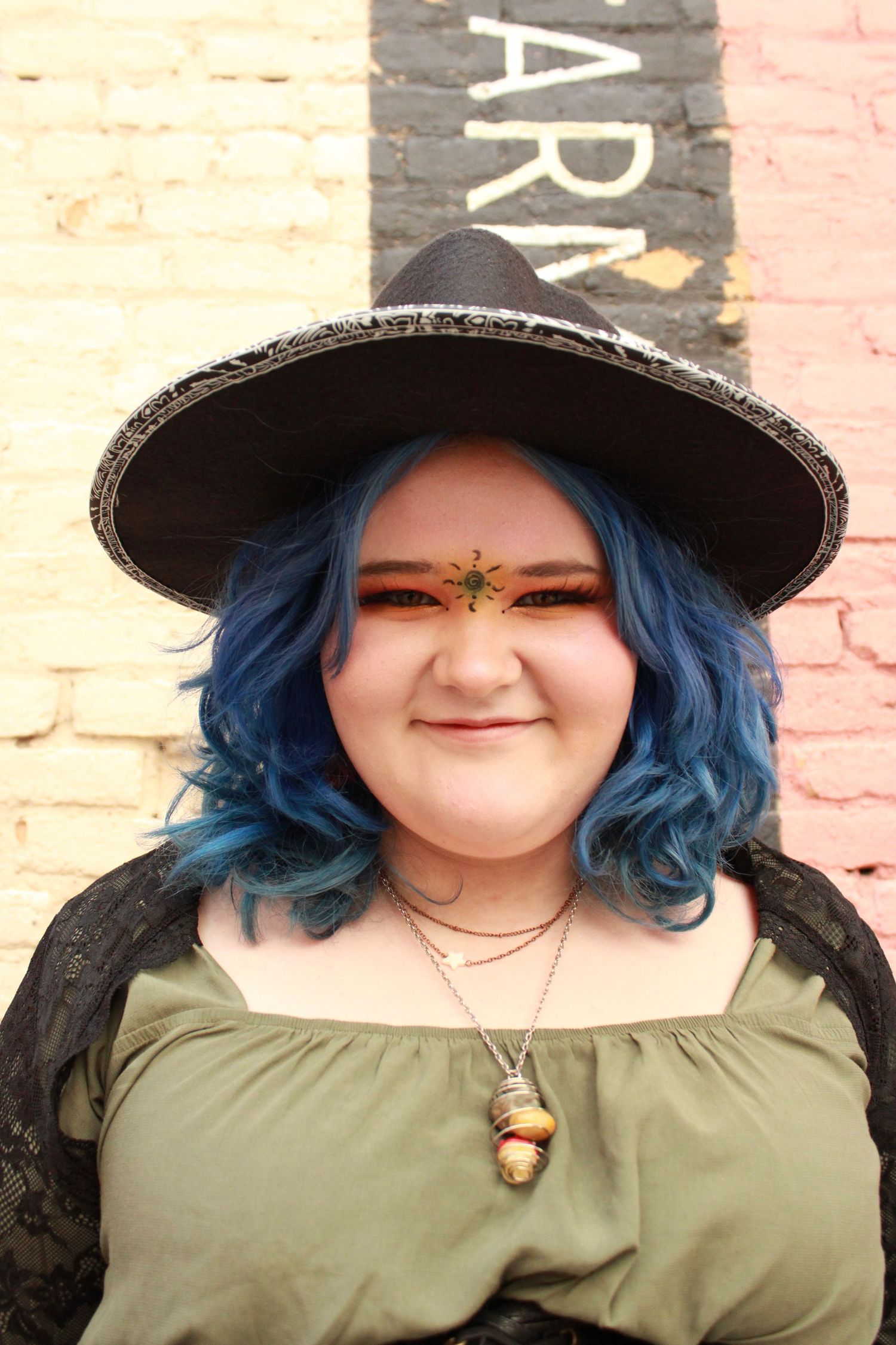 Close-up portrait with blue hair and decorative face art wearing an olive green top.