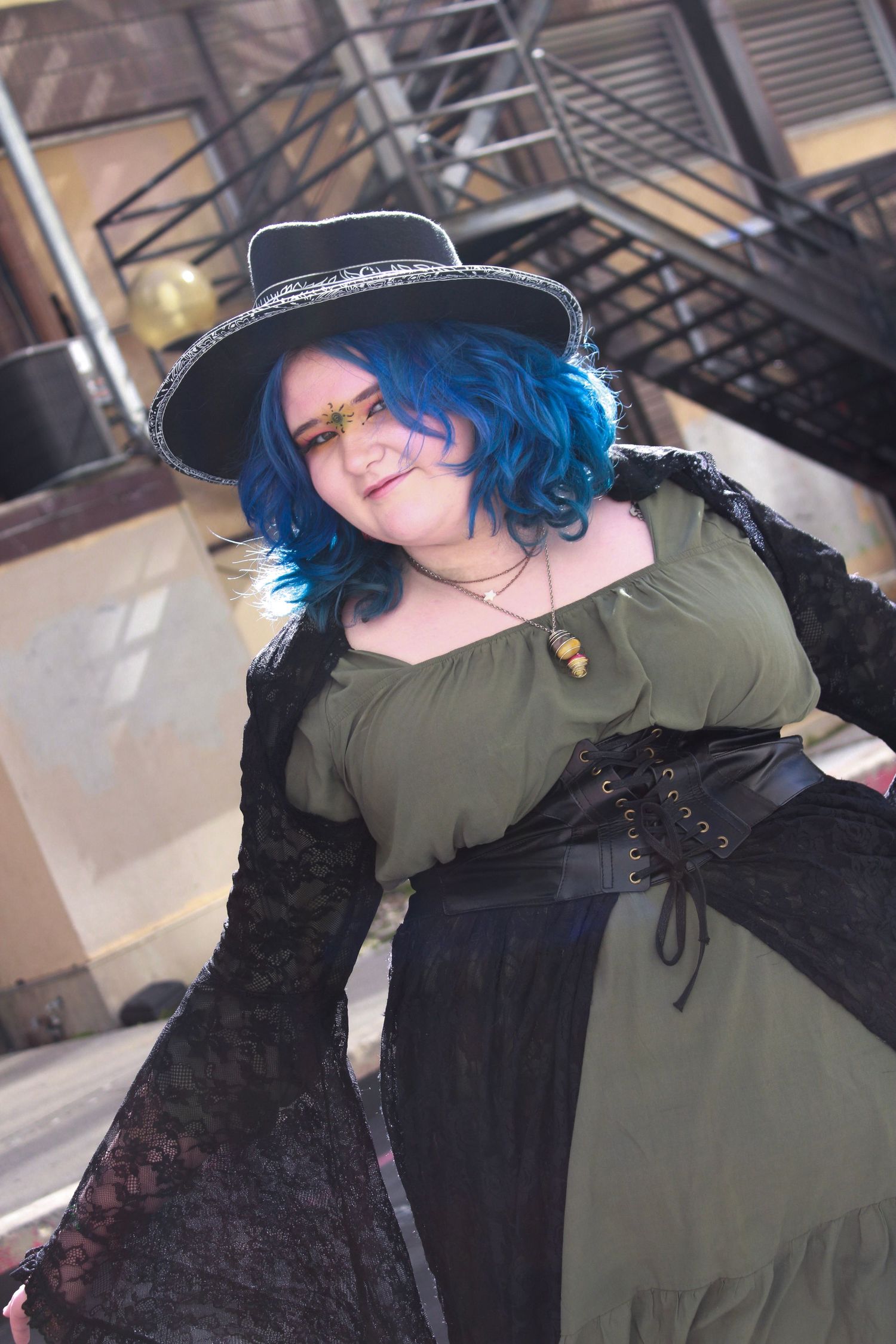 Stylish pose in medieval-inspired costume with blue hair against industrial background.