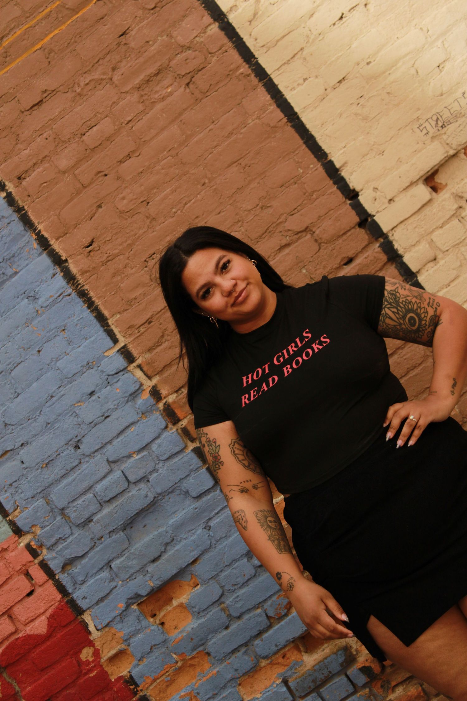 A casual portrait against a colorful brick wall wearing a black shirt with red text.