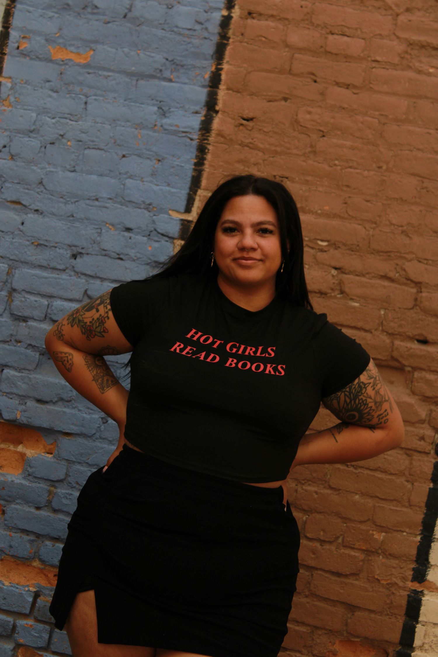 Stylish portrait against colored brick wall sections wearing a black t-shirt with red text.