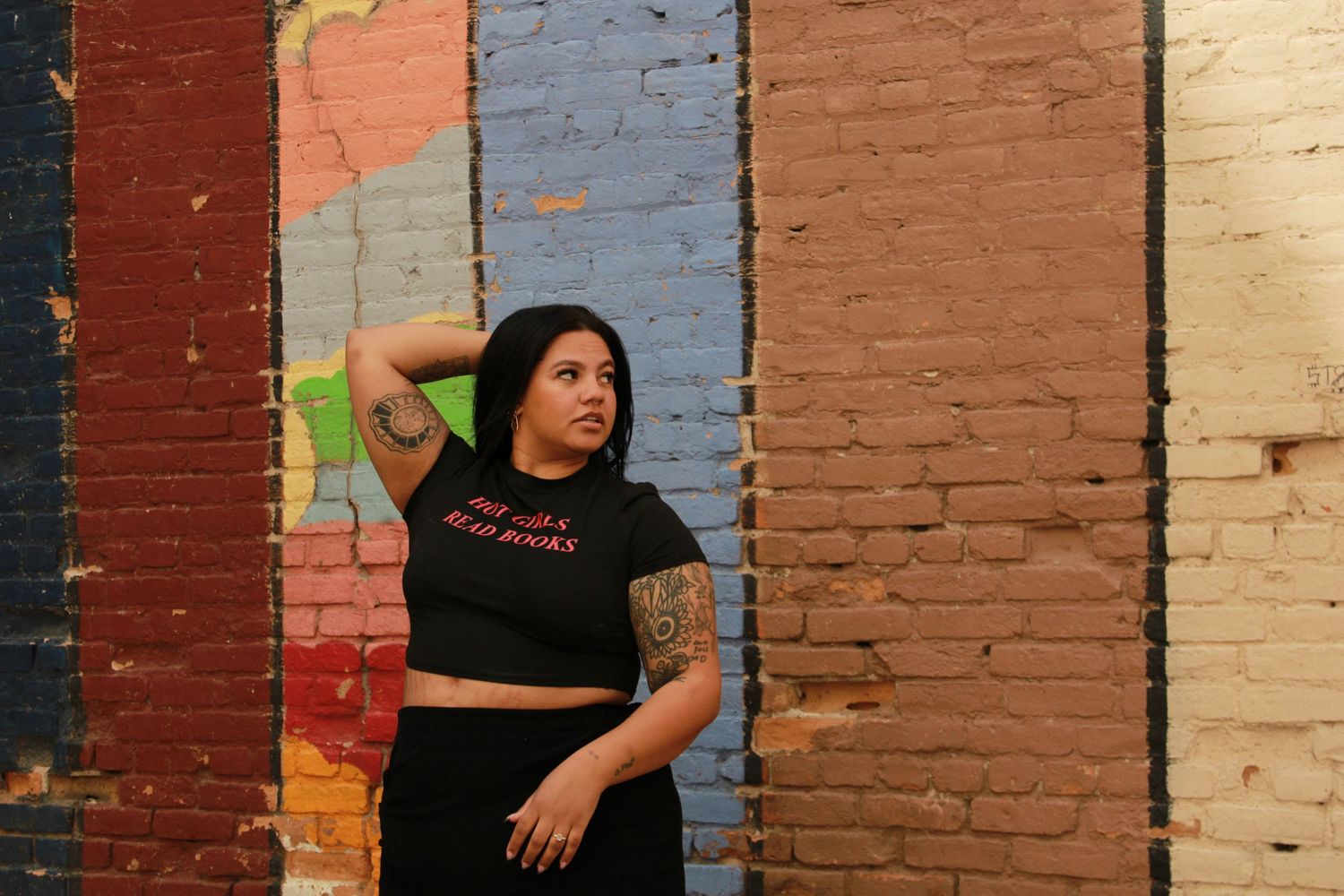 Artistic pose against painted brick wall sections wearing black crop top.