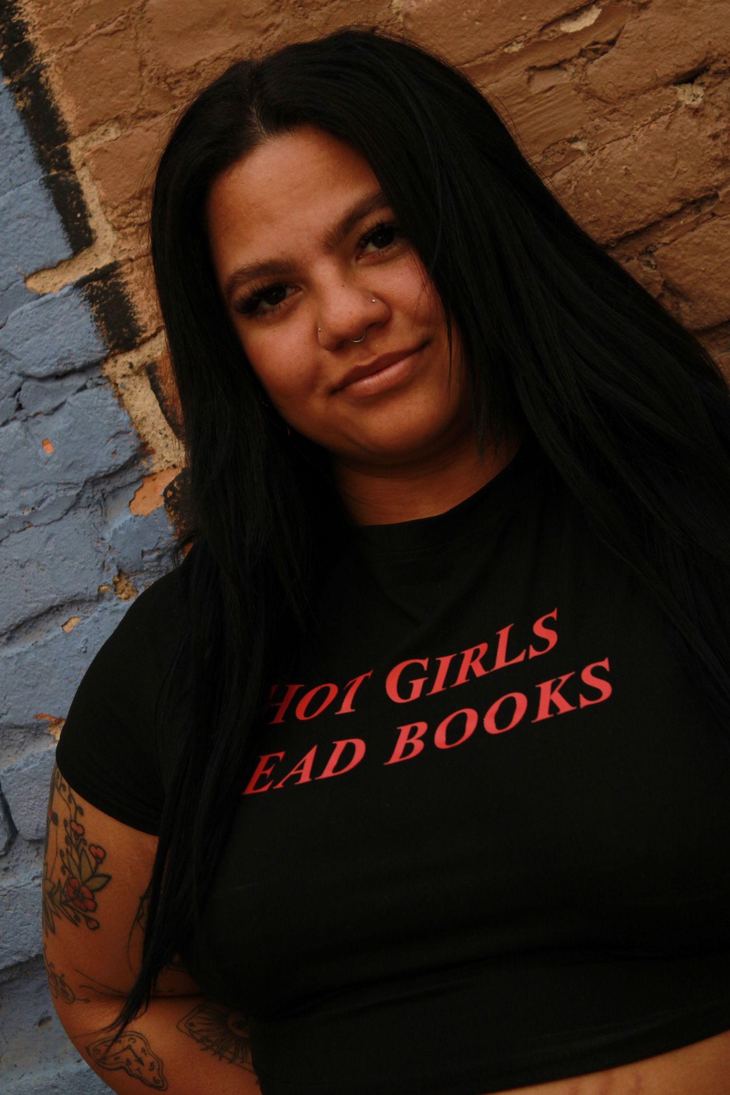 Close up portrait against blue and brown brick wall wearing black t-shirt with red text.