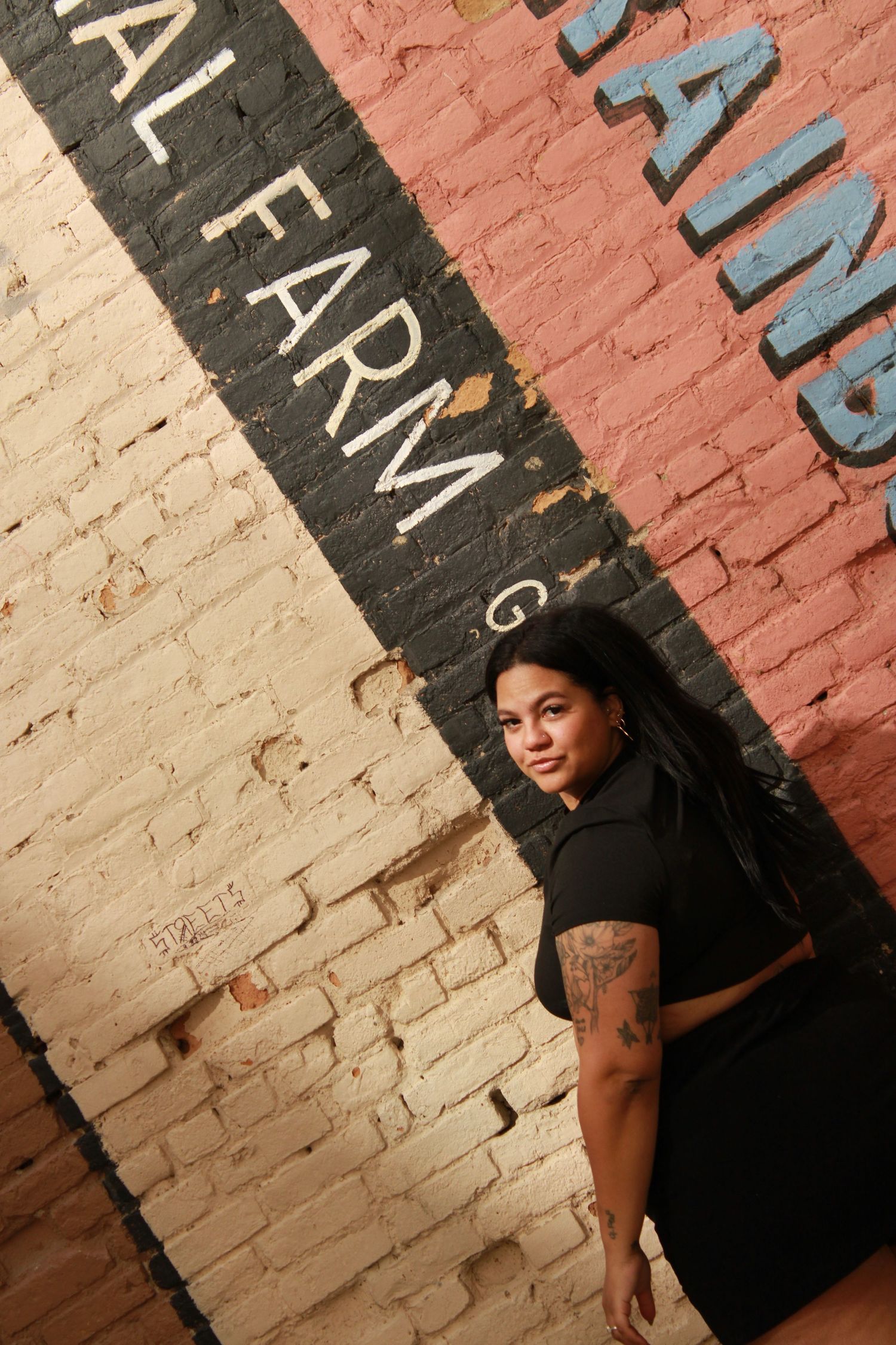 Artistic angle portrait near painted wall text wearing all black outfit.