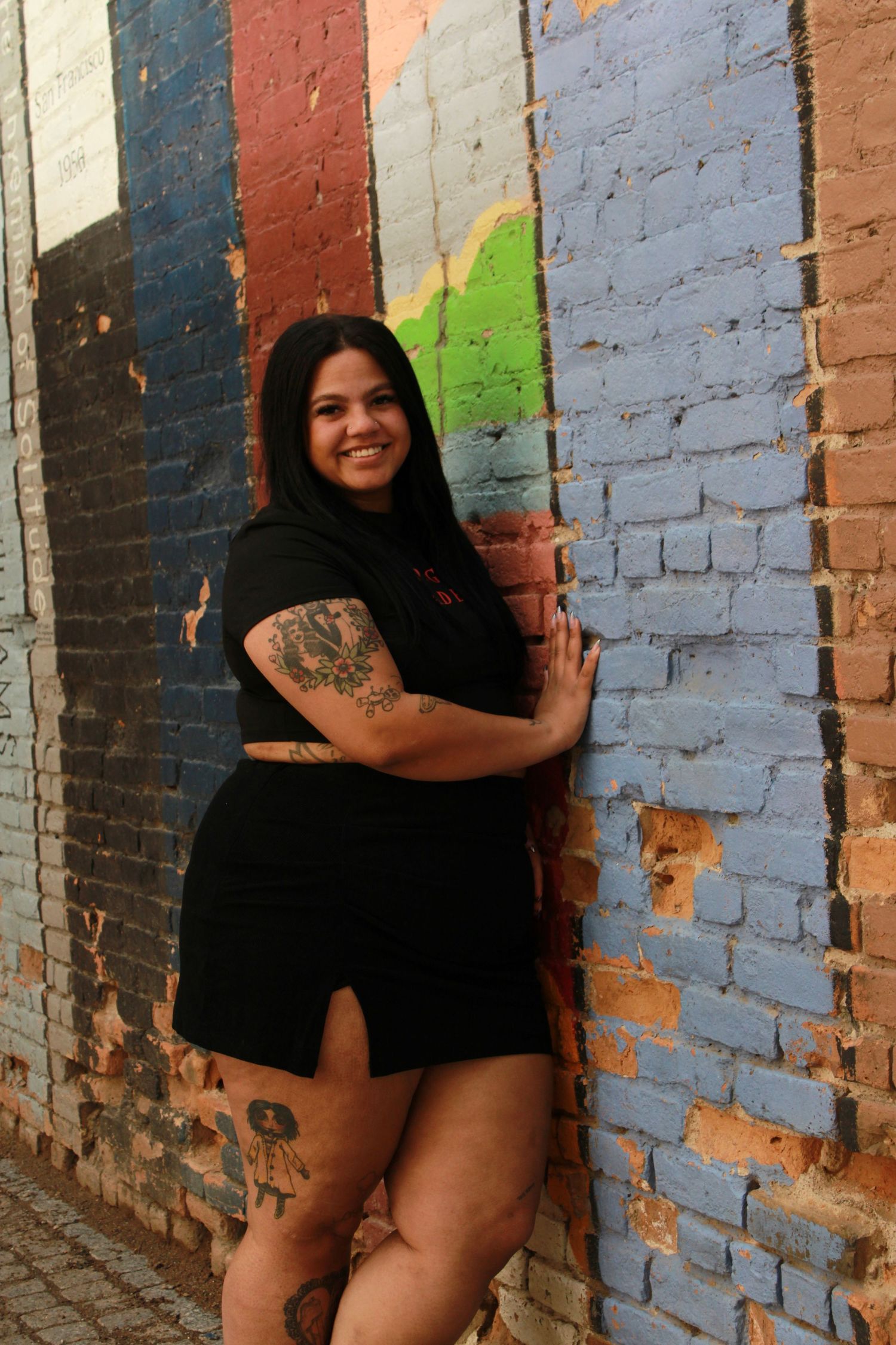 Person in black outfit poses near vibrant book-themed street art mural.